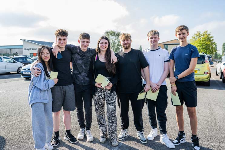Seven Tewkesbury A Level students stand facing the camera with their results in hand