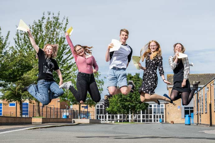 Five students jump into the air with joy holding their GCSE results
