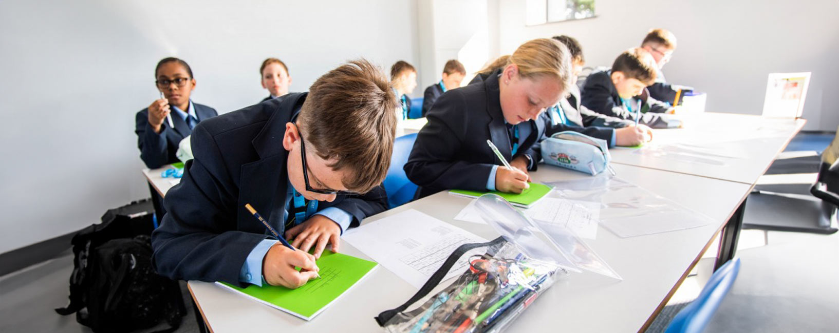 4 students sat in a classroom writing in green books